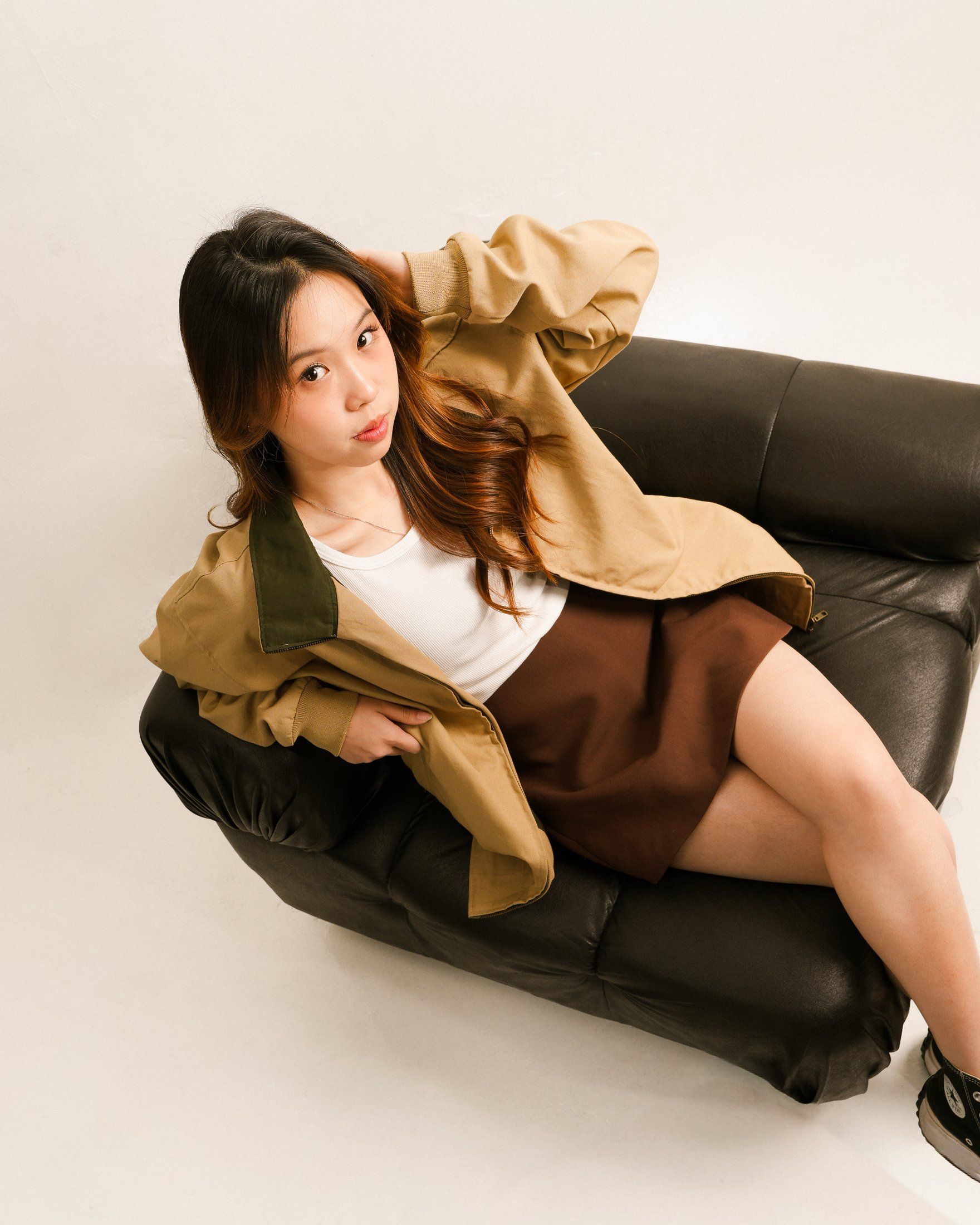 Model leaning back on a leather sofa in a relaxed khaki jacket