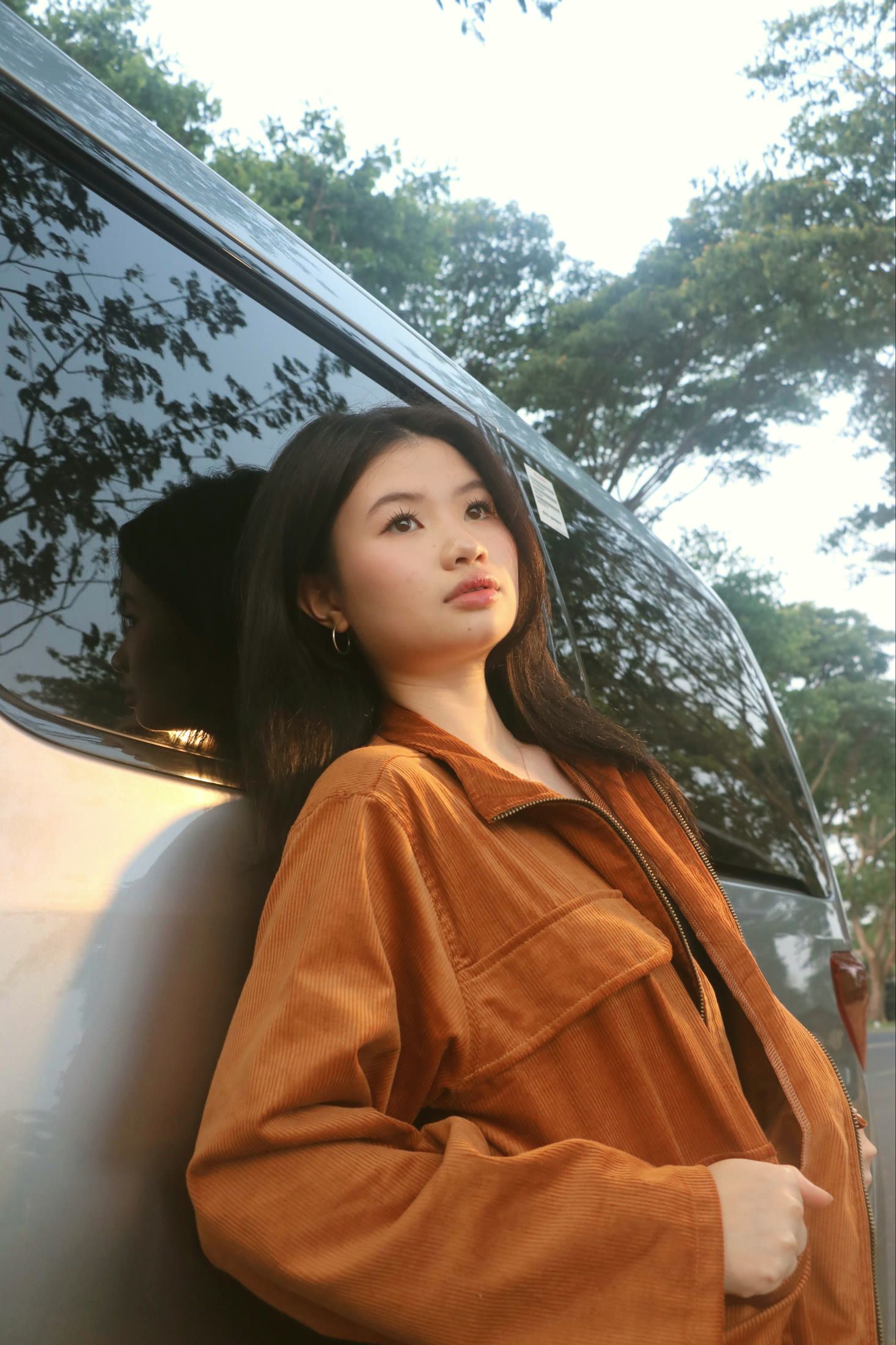 Model leaning on a car in the caramel longneck jacket