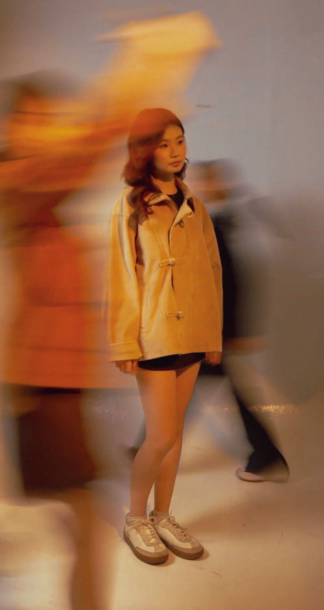 Model standing still in the cream cheongsam jacket as people blur past